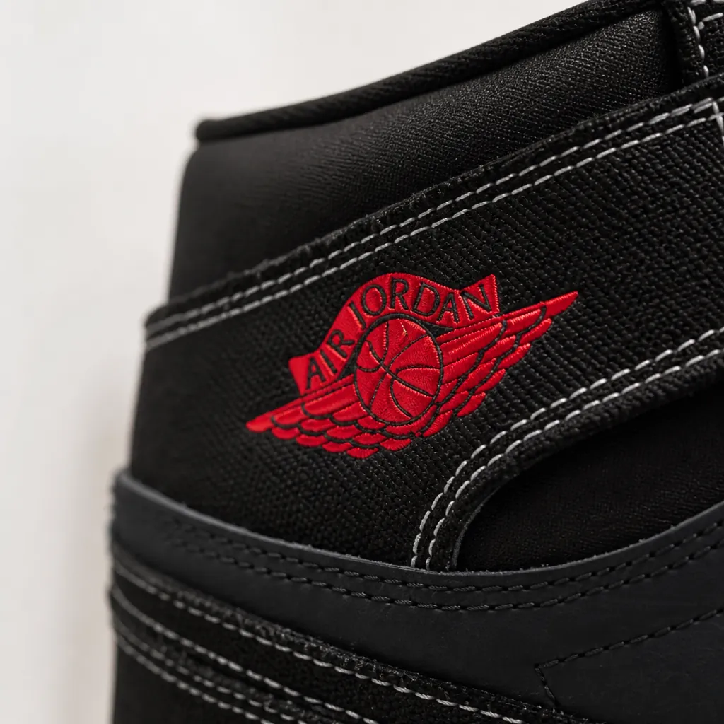Close-up macro shot of the premium black woven textile upper of the Air Jordan 1 Flight Club with crisp University Red accent stitching and the iconic Jumpman logo