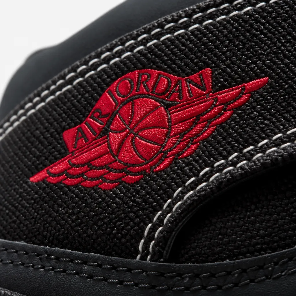 Extreme close-up of premium black woven textile upper showing intricate cross-hatch pattern with white and University Red accent stitching