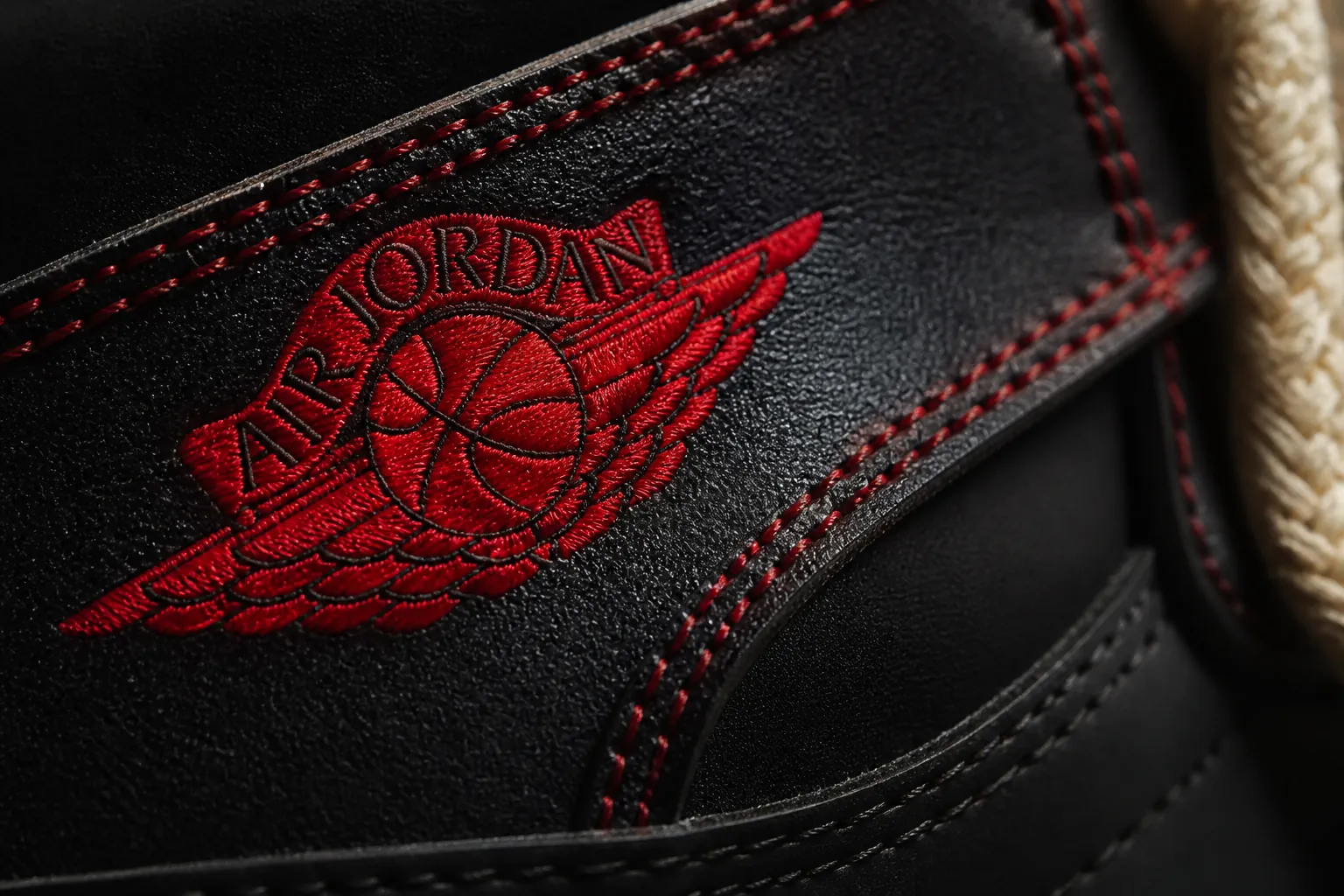 Macro photograph of University Red accent stitching and decorative elements showing premium red thread on black leather background